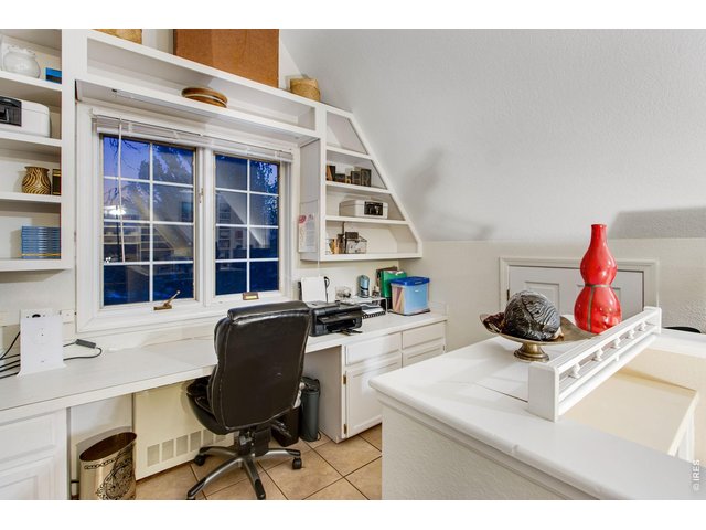 Property Photo 35 Office workstation with tile flooring, built-in wrap-around desk facing out the window. Built in shelving around the desk and bright overhead light. 