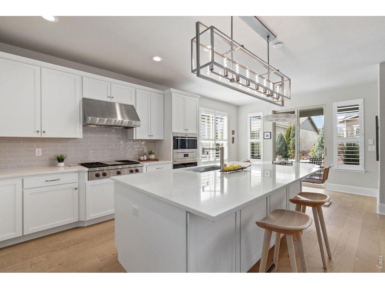 At the center of the home, a grand quartz island anchors a chef-inspired kitchen designed for both entertaining and everyday indulgence. White shaker cabinetry with soft-close detail, designer lighting, tile backsplash creates a clean tailored aesthetic.