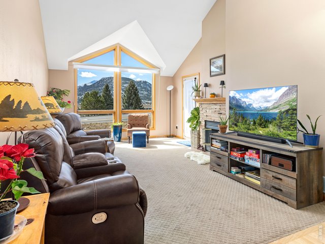 Property Photo 9 The living room showcases vaulted ceilings, a gas fireplace, and dramatic floor-to-ceiling windows that frame breathtaking views of the tallest peaks in Rocky Mountain National Park.