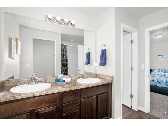 Property Photo 14 The primary ensuite bathroom features dual sinks, set within rich dark cabinetry that provides ample storage and complements the soft light-colored walls. The shower tub combo is ideal for quick routines and relaxing soaks! 