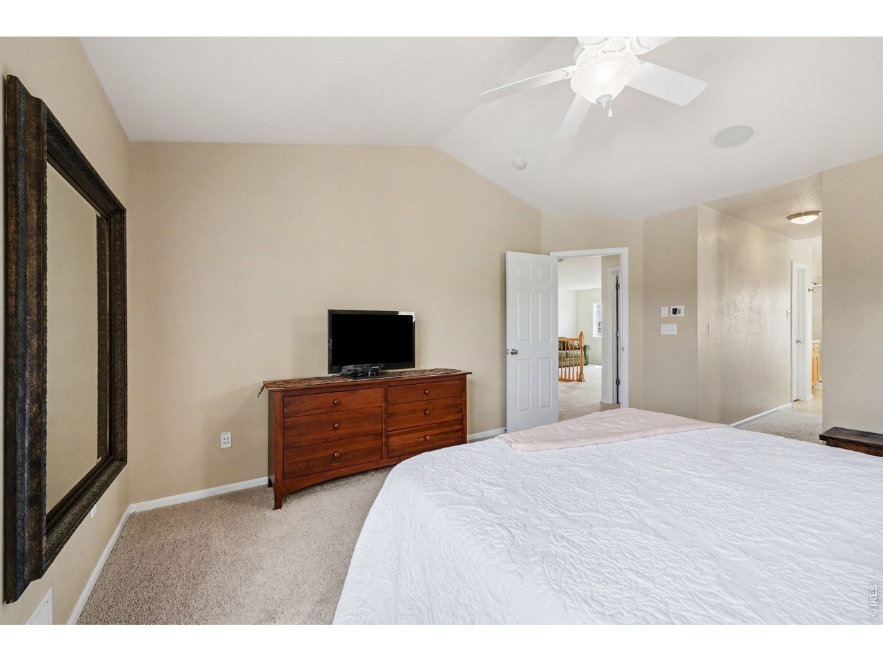 Spacious primary retreat with vaulted ceilings, a large accent mirror, and plenty of room for a full entertainment setup