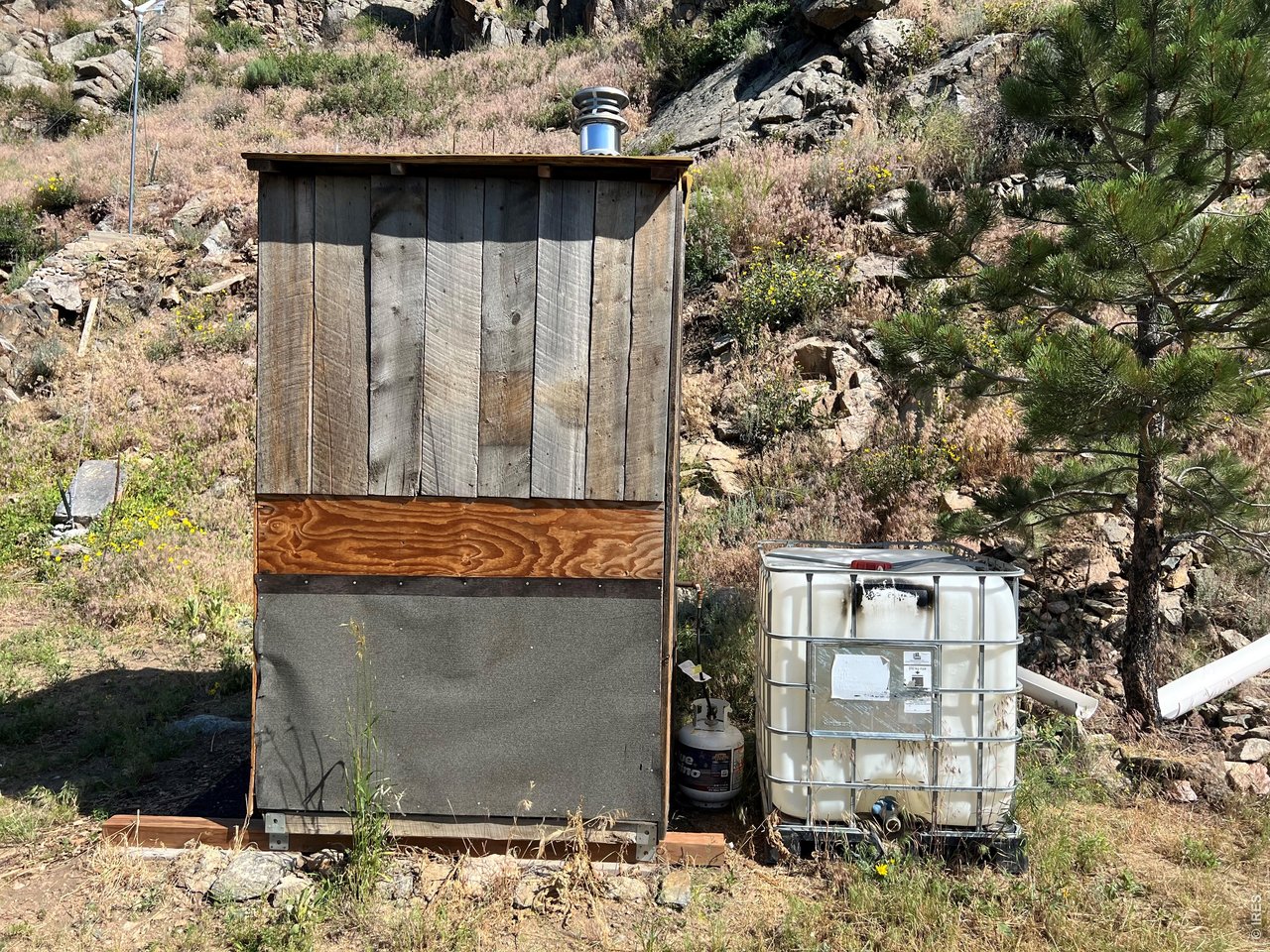 Side view of outhouse with one of the two 250-gallon water cisterns
