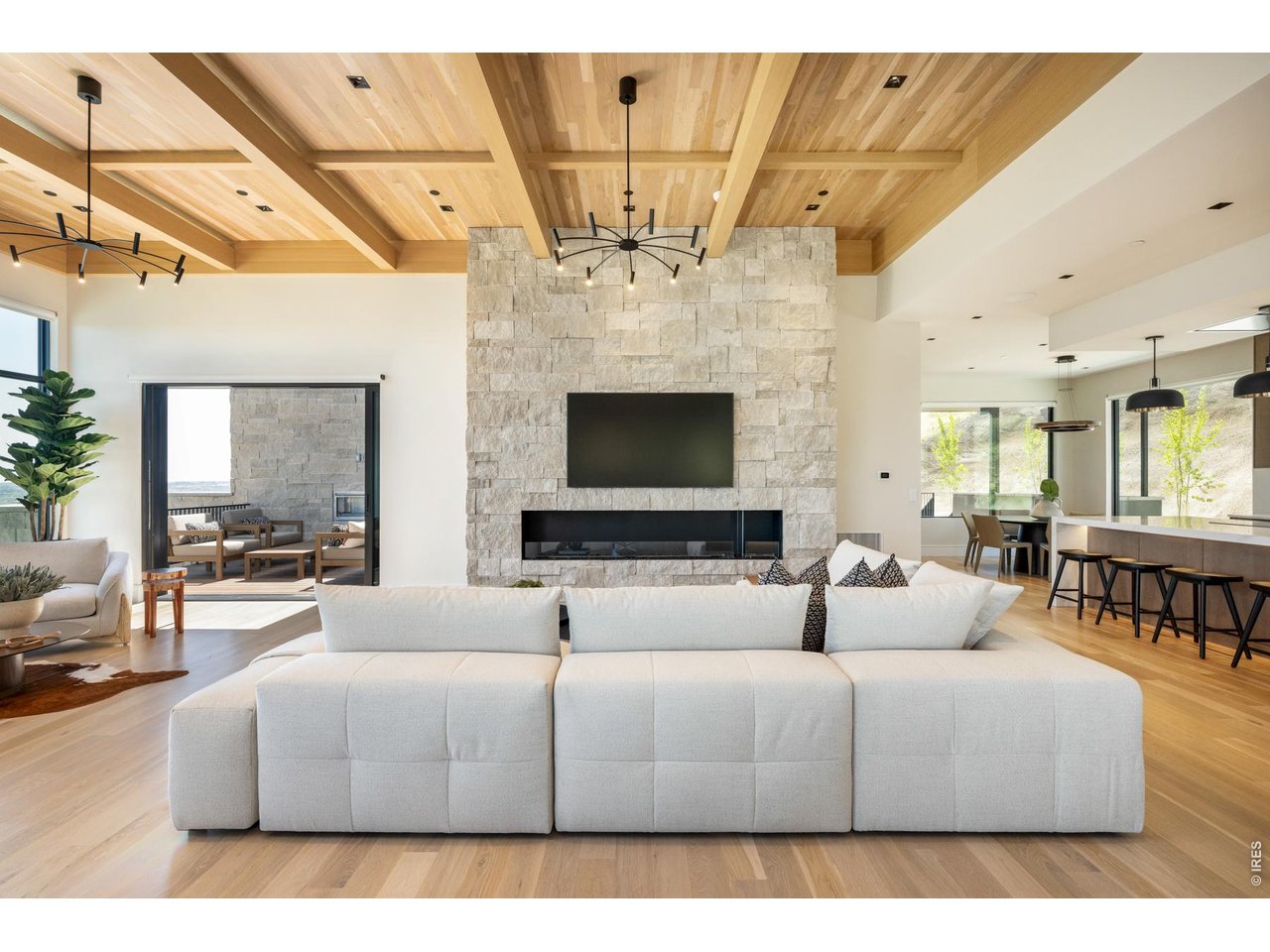 Oversized, sun-filled living room with stunning architectural beams anchored by designer pendant lighting and an EcoSmart Flex Series gas fireplace. 