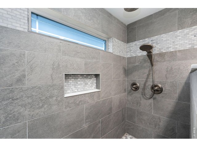 Property Photo 18 Modern tiled walk-in shower featuring a sleek dual-head system with a wall-mounted rain shower and handheld wand. Incredible tile work with mosaic accent niche and clerestory window.