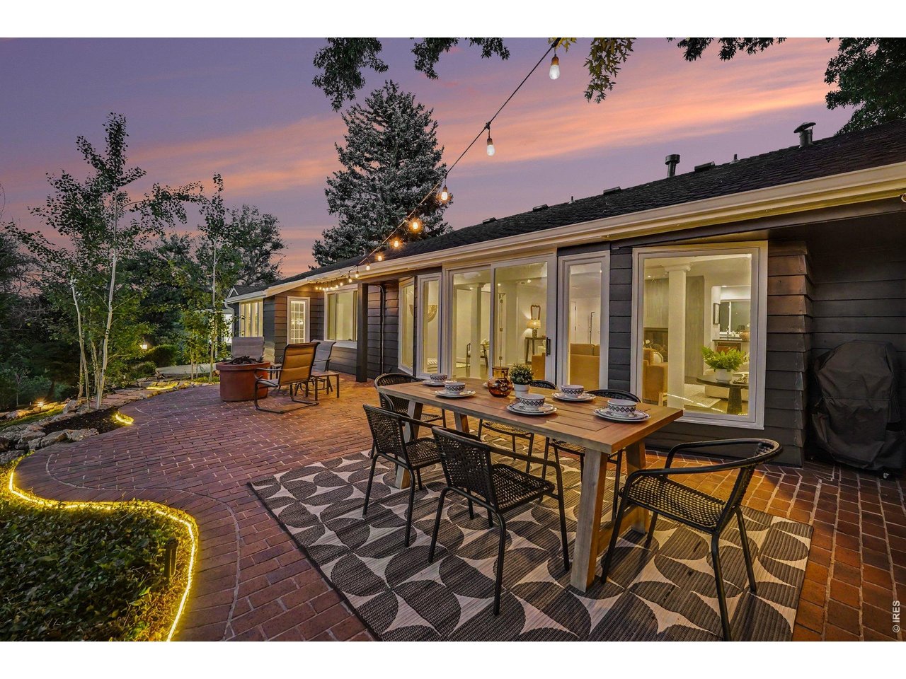 Host epic gatherings on this premium brick patio, perfectly framed by a brilliant twilight sky, mature trees, and warm, inviting indoor spaces.