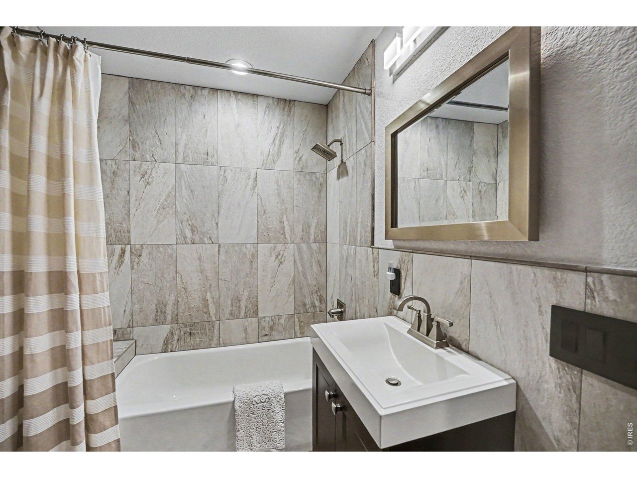 Beautifully remodeled secondary bathroom. Features a modern espresso vanity with a crisp white basin sink, updated brushed nickel fixtures, and a stunning custom floor-to-ceiling tile.