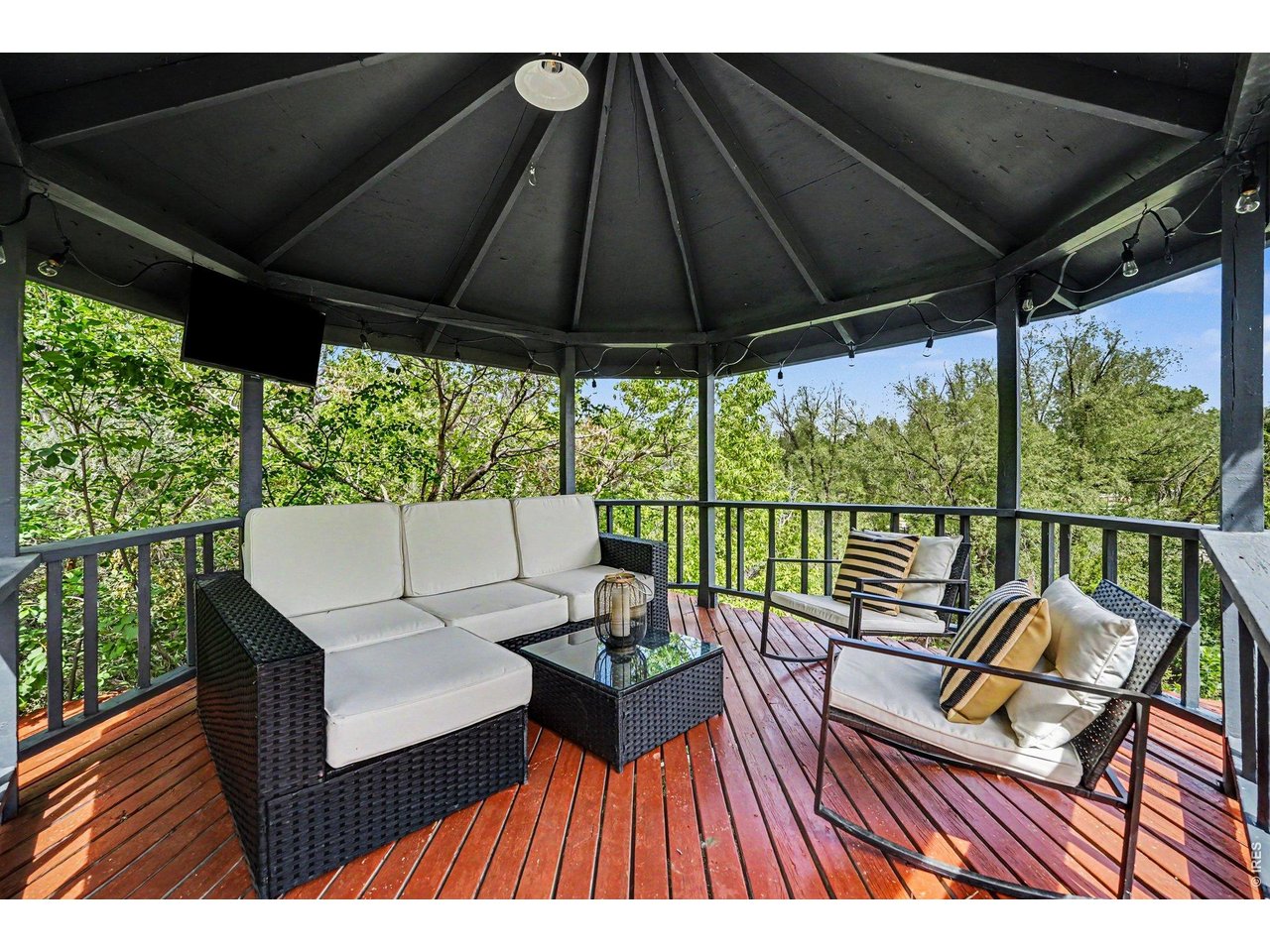 The ultimate outdoor lounge! Spectacular covered gazebo overlooks the lush, tree-lined acreage. Features natural wood decking, an integrated flat-screen TV mount, festive string lighting, and panoramic nature views.