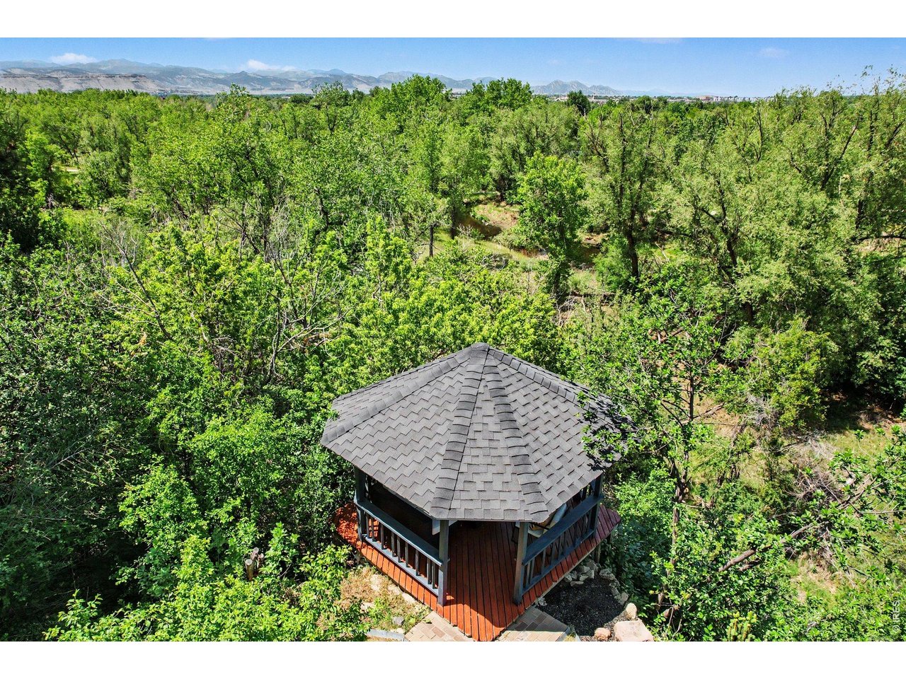 Private backyard gazebo nestled among lush, mature trees, offering a tranquil retreat with breathtaking mountain views on the horizon.