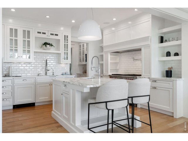 Property Photo 16 Chef's kitchen featuring bespoke cabinetry, marble countertops, a suite of Wolf, Sub-Zero, and Miele appliances, an oversized island, and a charming breakfast banquette. 