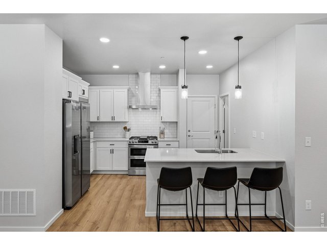 Property Photo 10 Stylish kitchen with stainless steel appliances, a dual-fuel gas range with vent hood, white maple cabinetry, subway tile backsplash, quartz countertops, pantry, and large breakfast bar