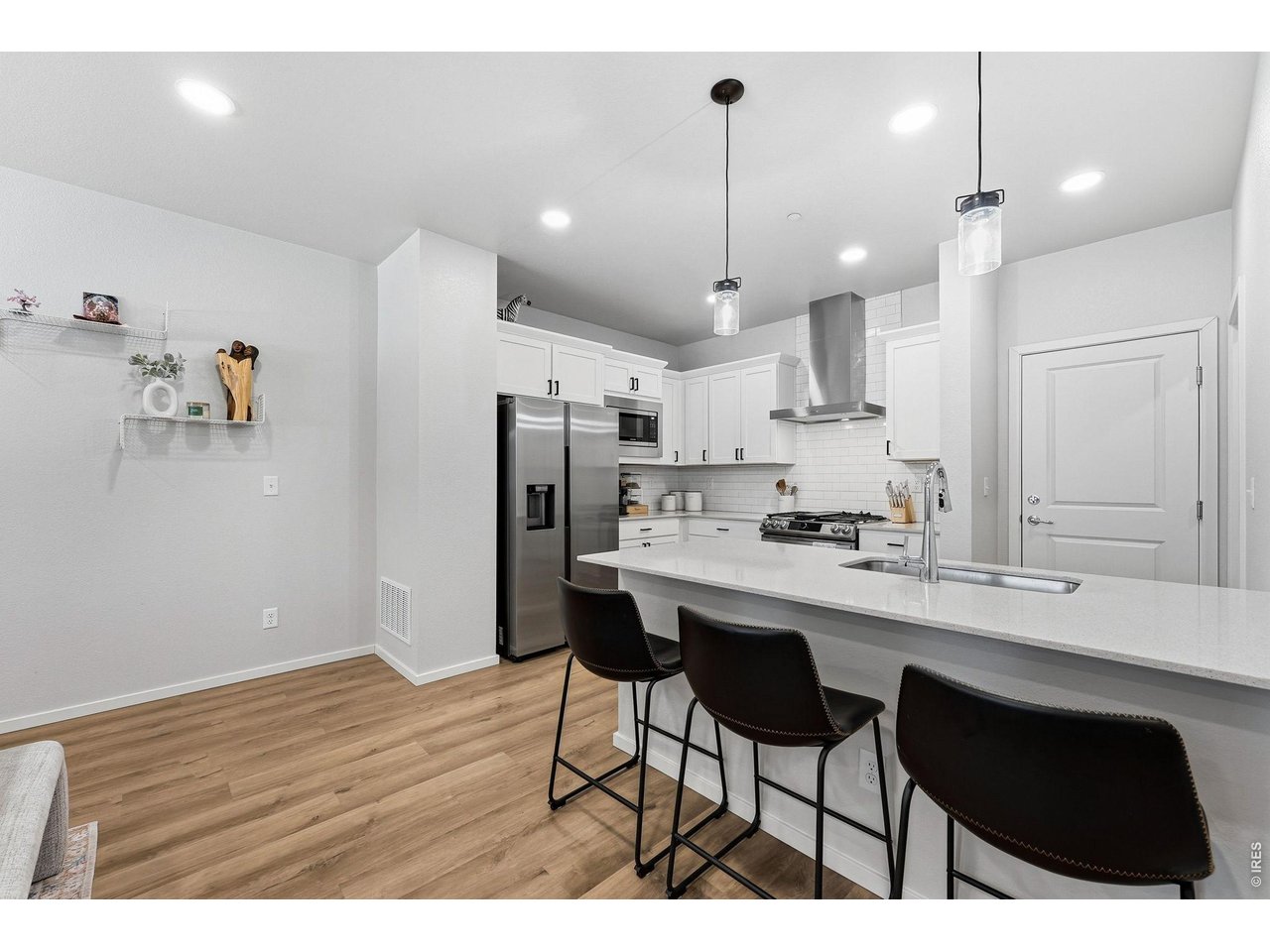 Stylish kitchen with stainless steel appliances, a dual-fuel gas range with vent hood, white maple cabinetry, subway tile backsplash, quartz countertops, pantry, and large breakfast bar