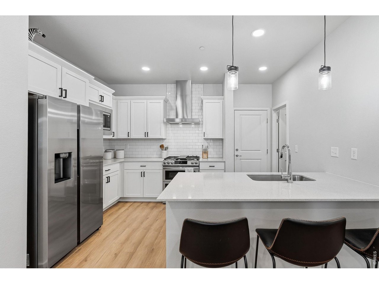 Stylish kitchen with stainless steel appliances, a dual-fuel gas range with vent hood, white maple cabinetry, subway tile backsplash, quartz countertops, pantry, and large breakfast bar