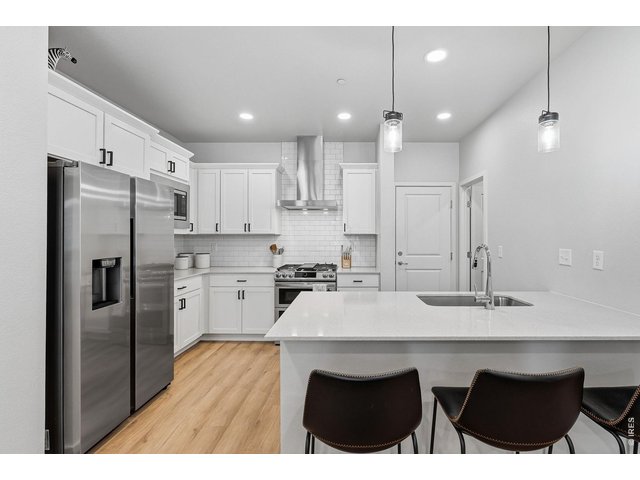 Property Photo 12 Stylish kitchen with stainless steel appliances, a dual-fuel gas range with vent hood, white maple cabinetry, subway tile backsplash, quartz countertops, pantry, and large breakfast bar