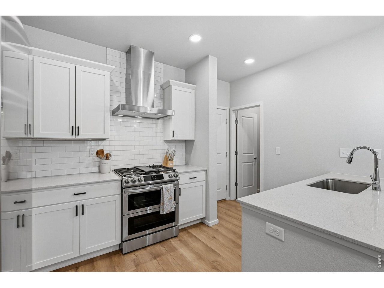 Stylish kitchen with stainless steel appliances, a dual-fuel gas range with vent hood, white maple cabinetry, subway tile backsplash, quartz countertops, pantry, and large breakfast bar