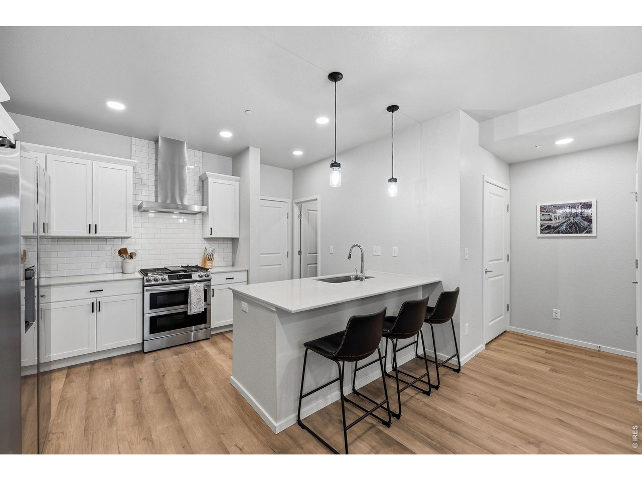 Stylish kitchen with stainless steel appliances, a dual-fuel gas range with vent hood, white maple cabinetry, subway tile backsplash, quartz countertops, pantry, and large breakfast bar