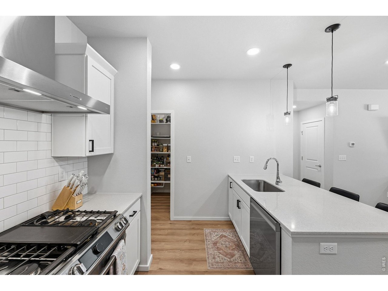 Stylish kitchen with stainless steel appliances, a dual-fuel gas range with vent hood, white maple cabinetry, subway tile backsplash, quartz countertops, pantry, and large breakfast bar