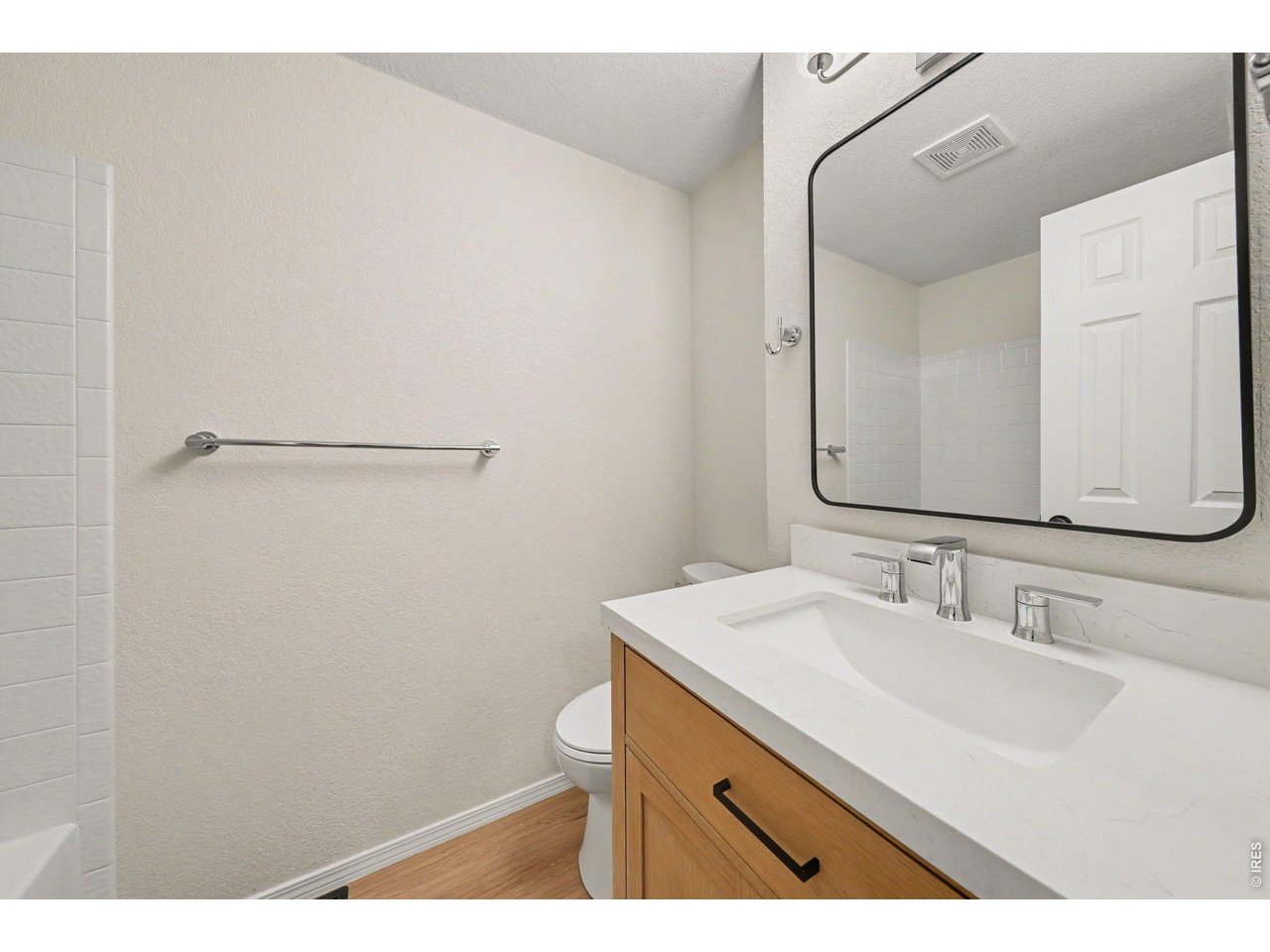 Property Photo 19 Clean, updated primary bathroom with a light-colored stone countertop, wood cabinetry, modern chrome fixtures, and a sleek black-trimmed mirror.