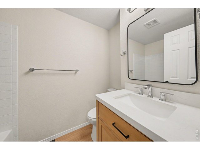 Property Photo 19 Clean, updated primary bathroom with a light-colored stone countertop, wood cabinetry, modern chrome fixtures, and a sleek black-trimmed mirror.