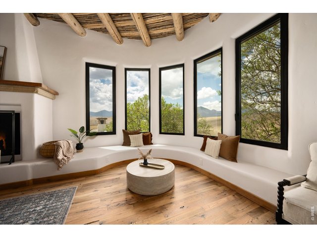 Property Photo 8 A warm and inviting living space featuring a striking wood-beamed ceiling, cozy fireplace, and panoramic windows that frame serene mountain views.