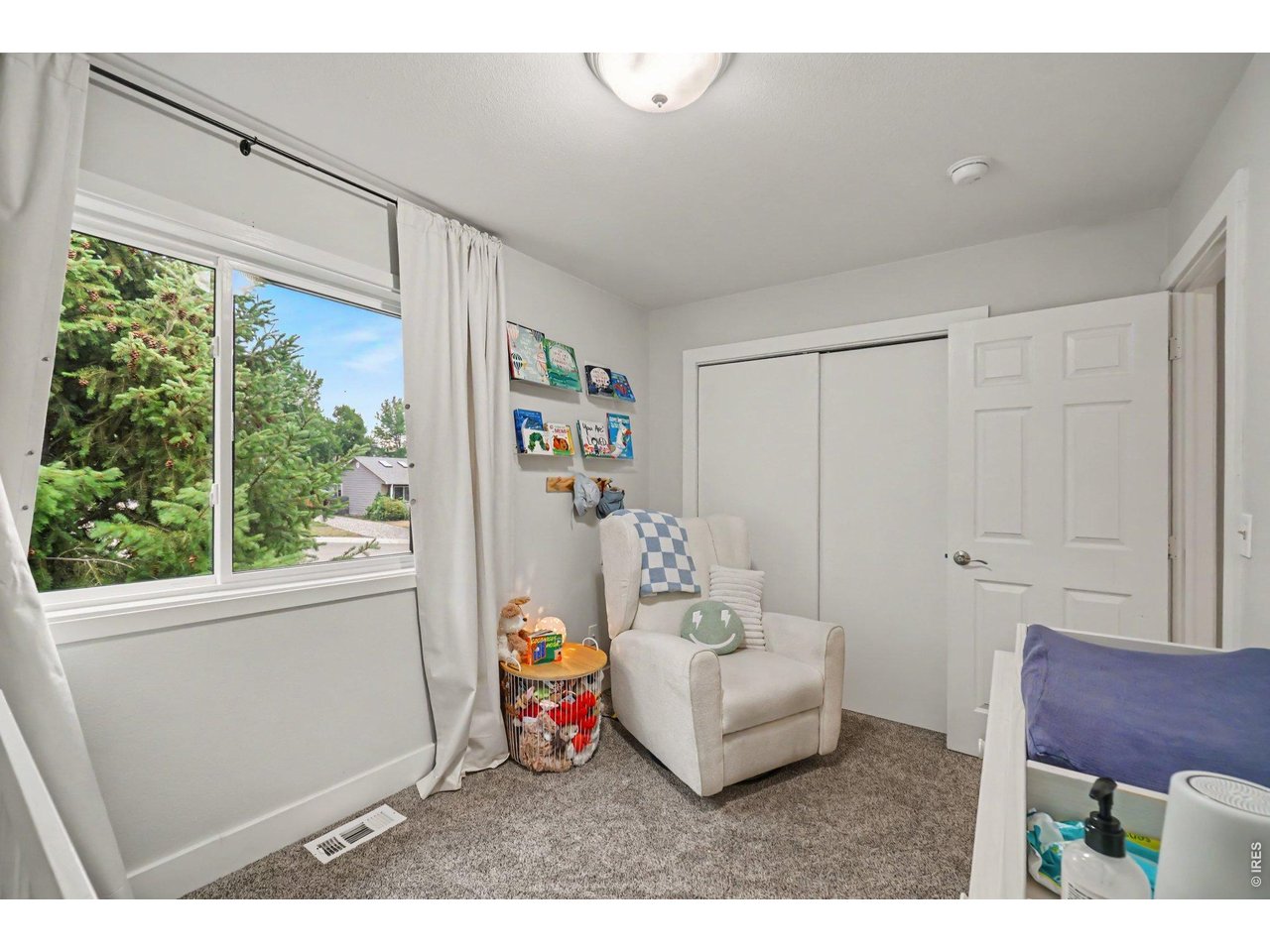 Property Photo 17 An inviting 2nd bedroom space featuring neutral tones, plush carpeting, a cozy reading nook, and a large window looking out to mature trees.