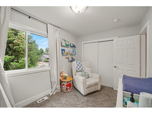 Property Photo 17 An inviting 2nd bedroom space featuring neutral tones, plush carpeting, a cozy reading nook, and a large window looking out to mature trees.