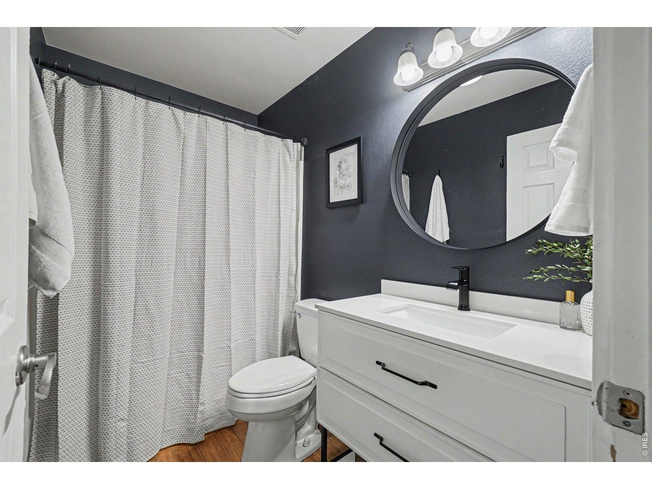 Property Photo 16 Full bathroom showcasing dramatic charcoal walls, a crisp white vanity with modern black hardware, and a sleek round mirror.