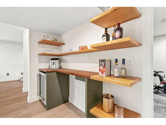 Property Photo 32 Stylish dry bar in basement with beverage fridge and custom lighting.