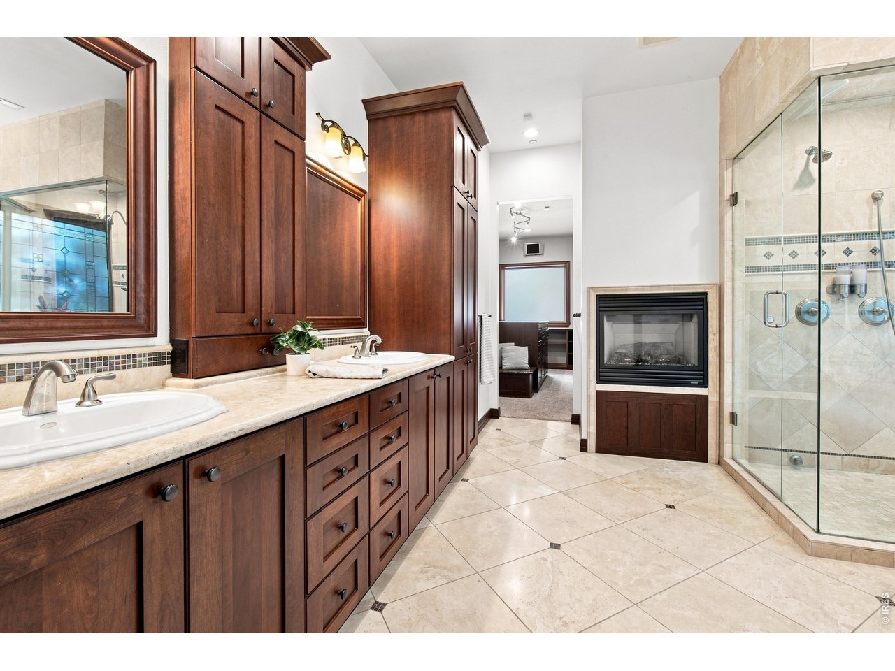 Property Photo 21 Spa-inspired primary bath featuring dual vanities, extensive cabinetry, oversized tiled shower and a cozy double-sided fireplace.