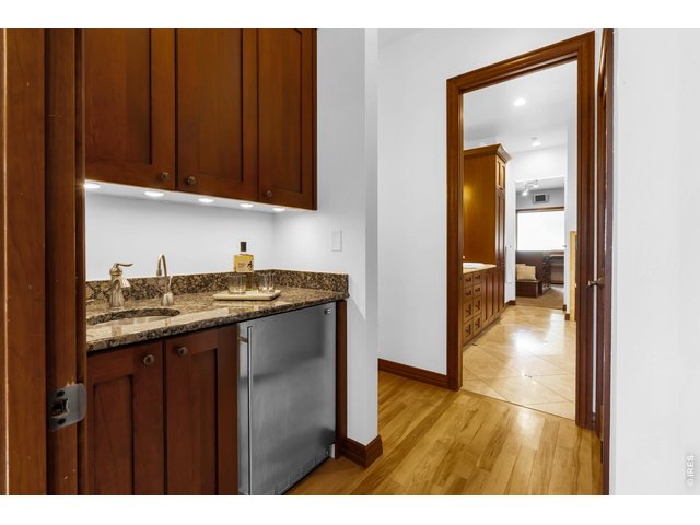 Property Photo 18 A grand entrance to the primary suite features a private beverage station with custom cabinetry, granite countertop, sink and under-counter refrigerator.