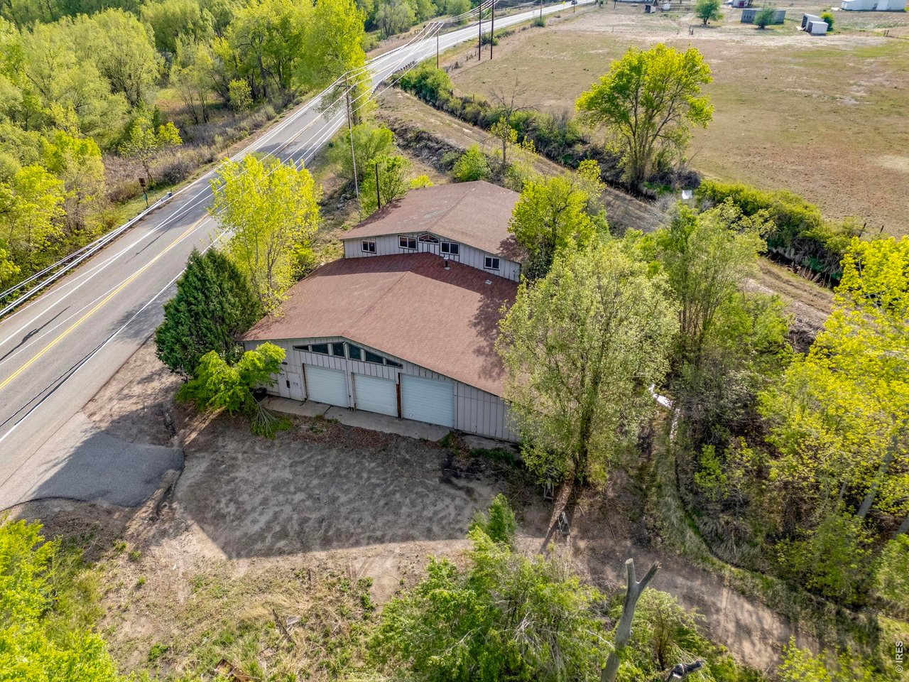Property Photo 28 Aerial view of the 7157 W Highway 34 residence and one of the property's larger outbuildings, with the Louden Ditch just beyond amid the mature trees.
