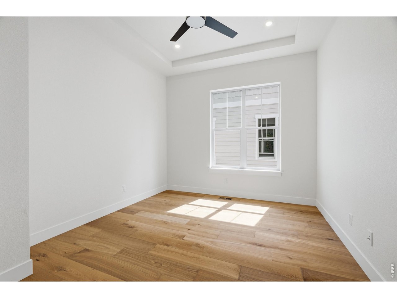 Property Photo 16 Main-level office or flex space with warm wood flooring and tray ceiling detail.