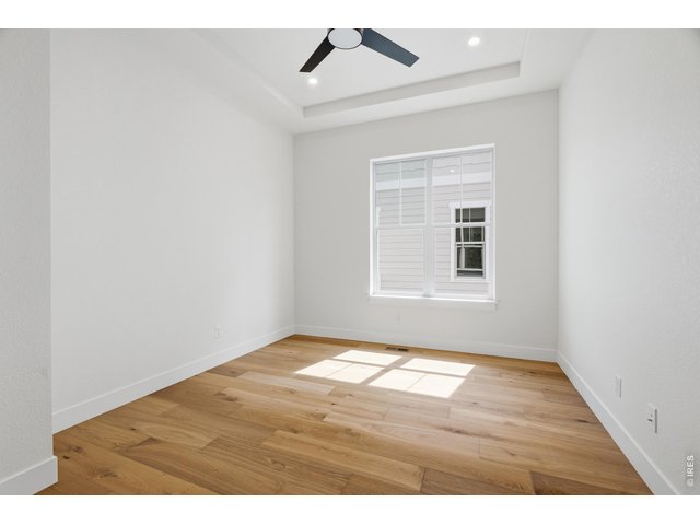 Property Photo 16 Main-level office or flex space with warm wood flooring and tray ceiling detail.