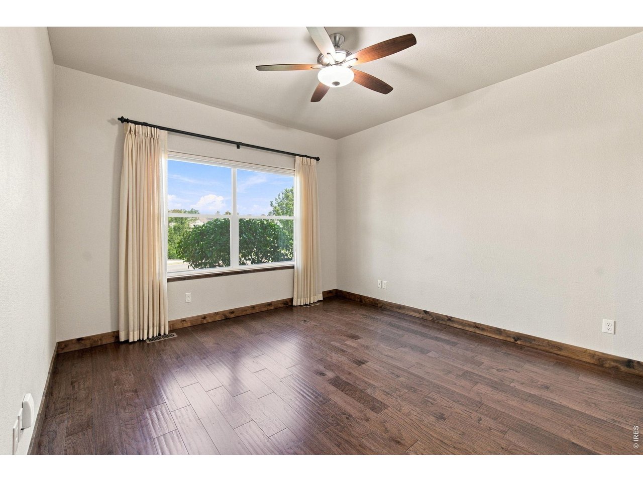 Property Photo 10 Spacious Primary main-level bedroom with hardwood flooring, ceiling fan and a large window providing wonderful natural light.