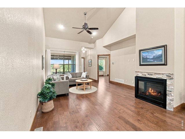 Property Photo 12 Warm and welcoming living space featuring a gas fireplace with stone surround, vaulted ceiling and beautiful hardwood flooring.