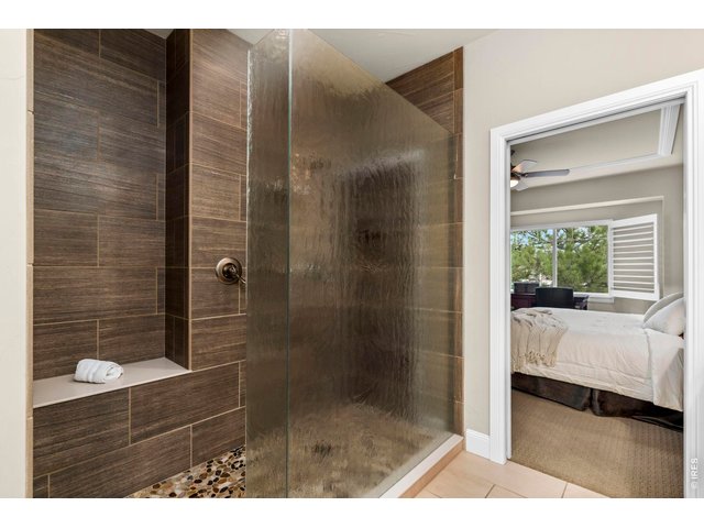 Property Photo 11 This primary suite bathroom features a luxurious walk-in shower complete with multiple adjustable shower heads, a custom pebble stone floor, and premium designer tiles to create a relaxing spa-like retreat.