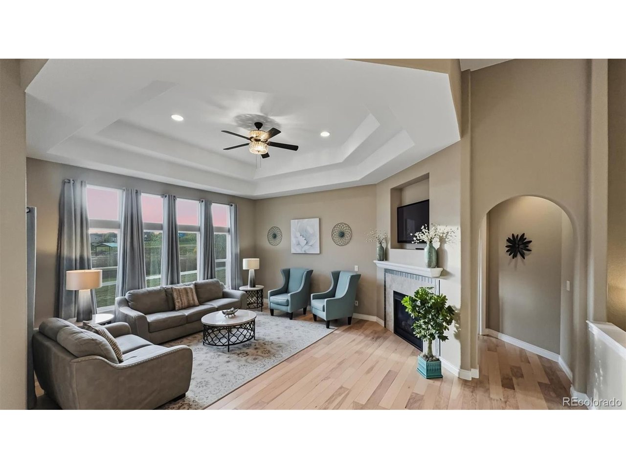 Elegant Living Room with tray ceiling, lighted ceiling fan, and wall of windows with backyard views.