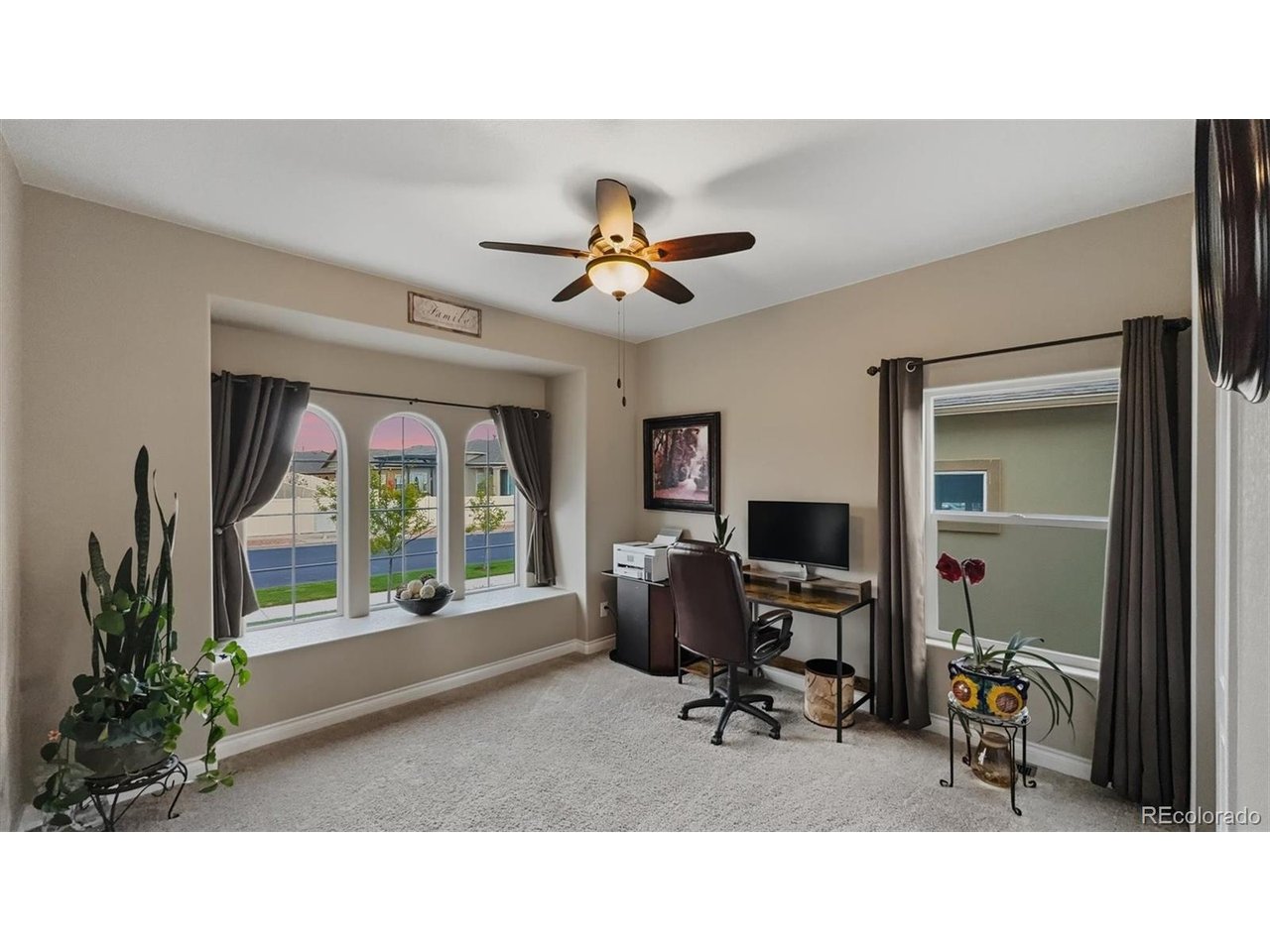 Main Level Bedroom #1 - currently an office with neutral carpet, lighted ceiling fan, arched windows and window seat.