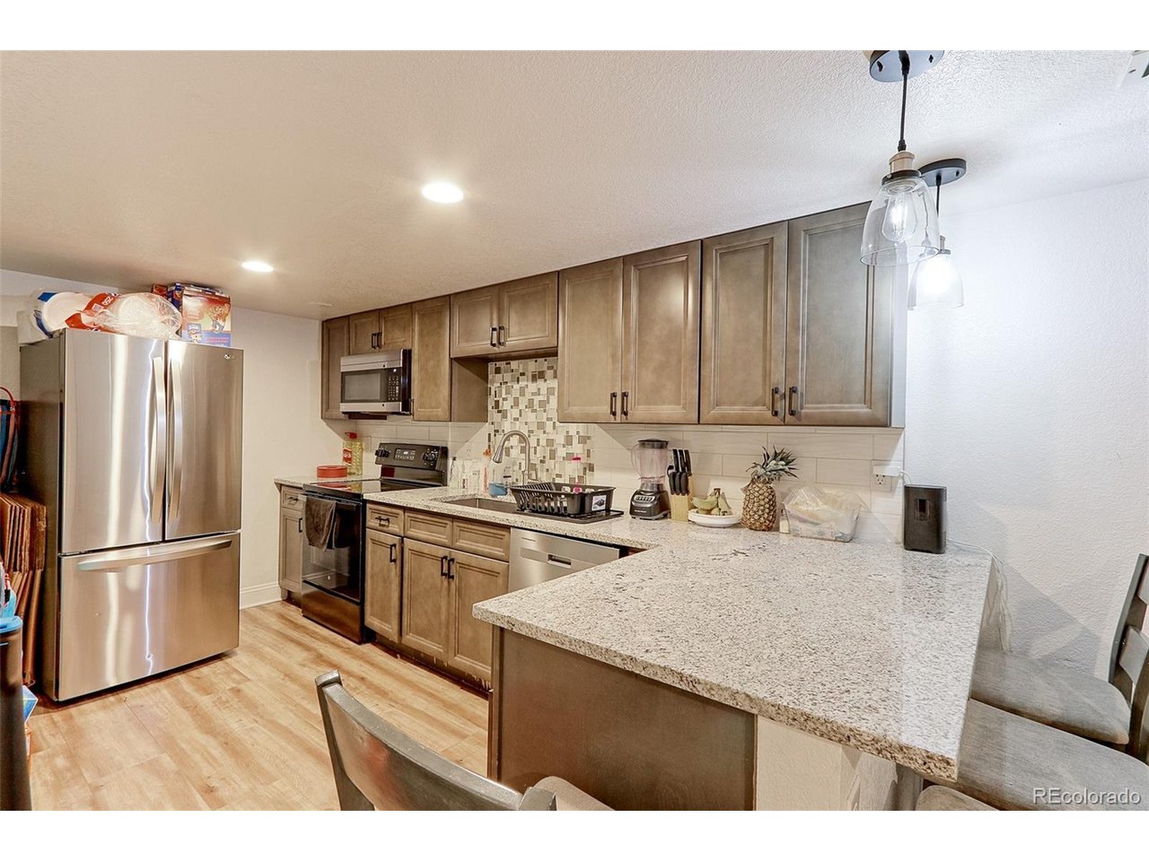 The 12x8 basement kitchen features LVP flooring, custom glazed raised panel cabinets with designer bronze pulls, solid granite countertops, designer tile backsplash, double deep stainless-steel integrated sink and upgraded stainless appliances that include